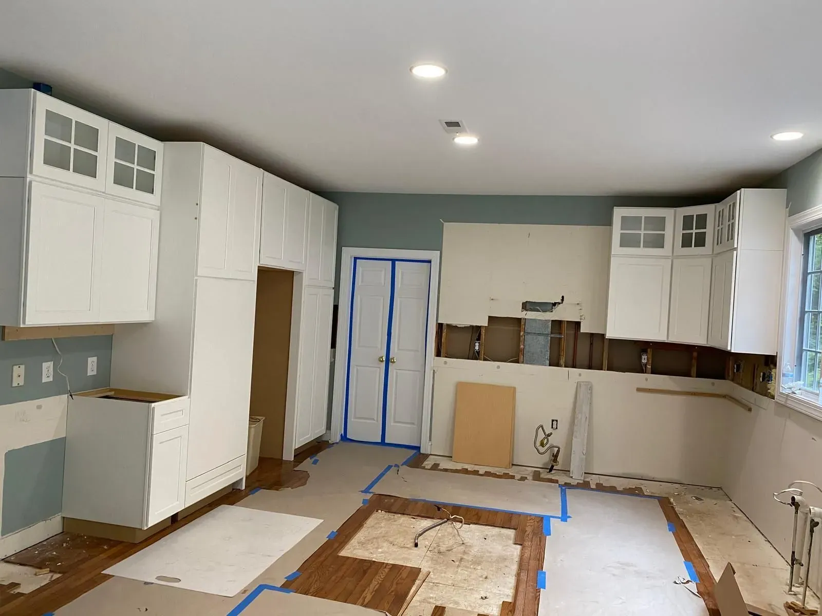 Partially renovated kitchen with white cabinets, blue painter’s tape, and unfinished flooring