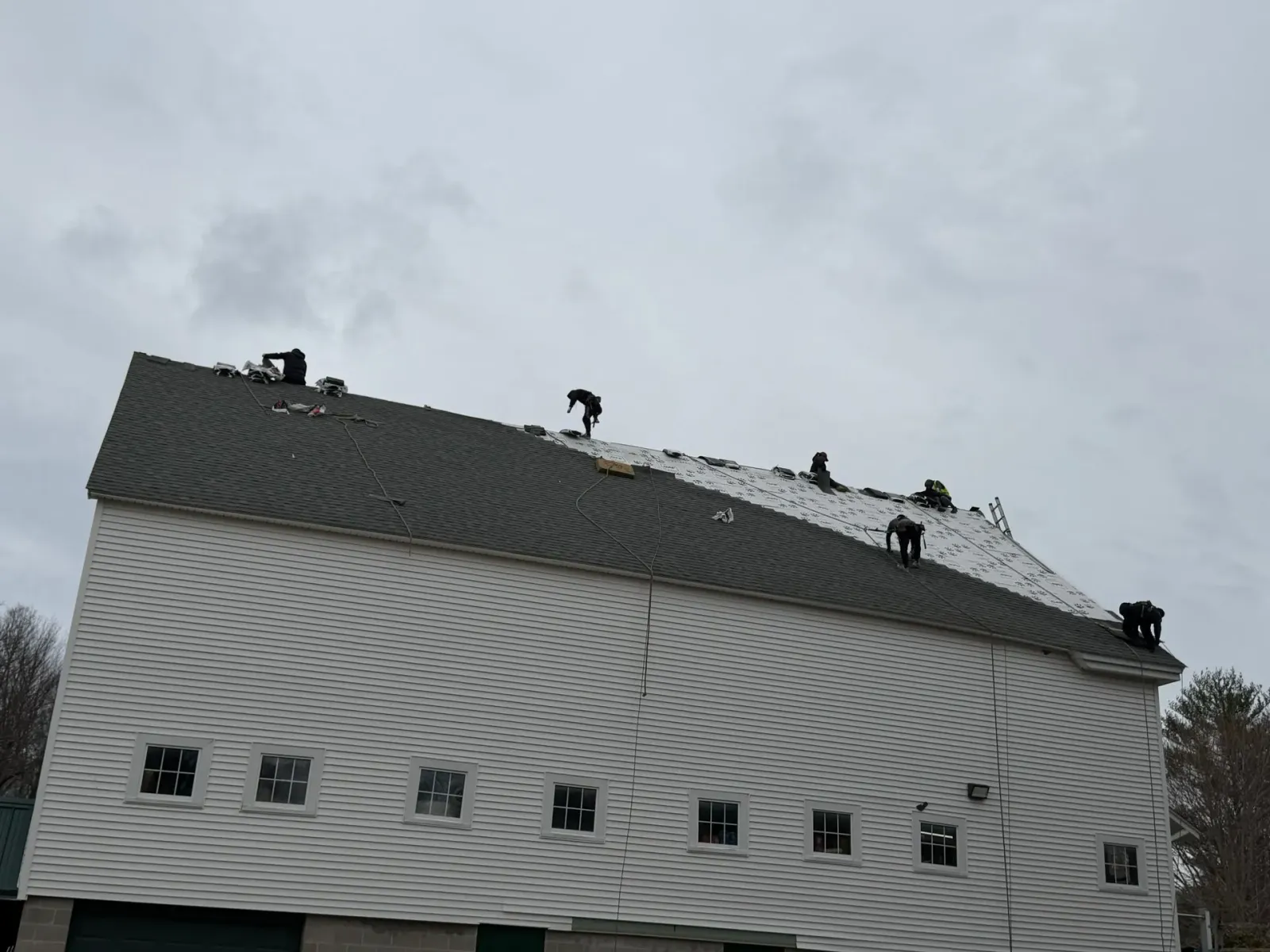 White house with a steep roof and several roofers working on top under a cloudy sky