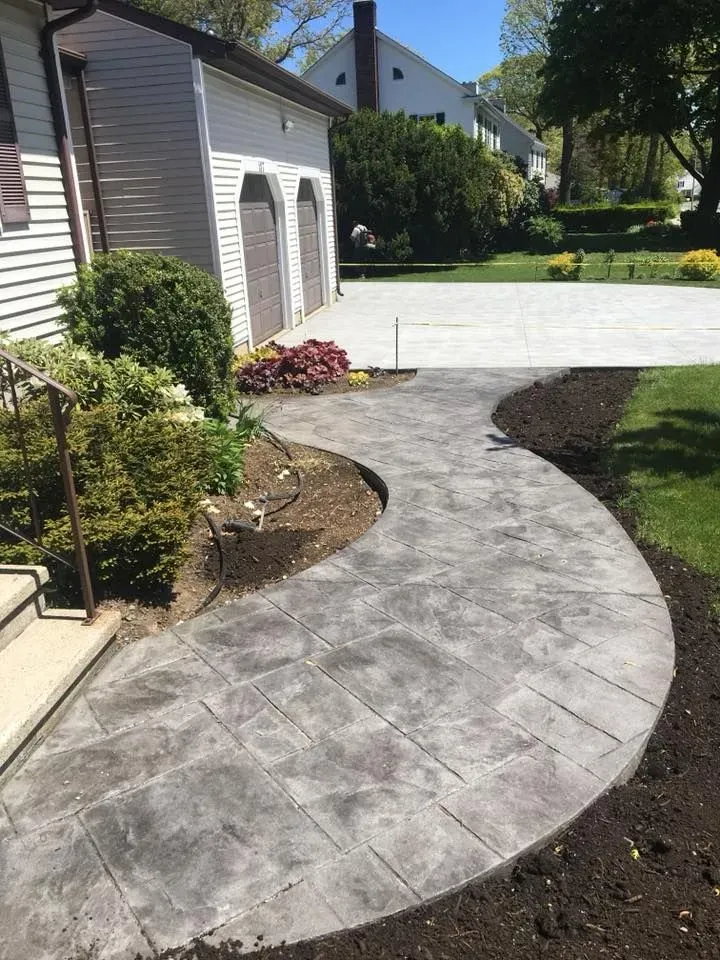 A concrete walkway leading to a garage next to a house.