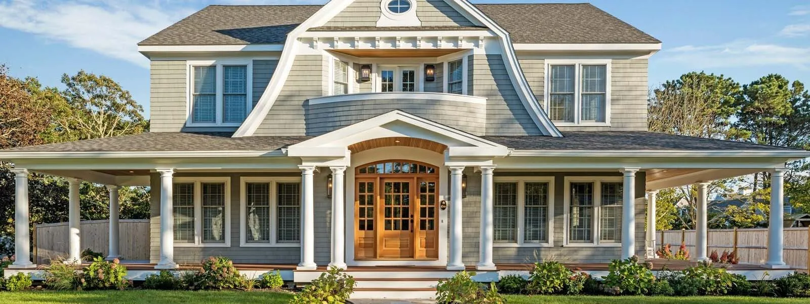 Two-story gray house with white trim and columned porch, manicured lawn – McPhee Associates of Cape Cod.