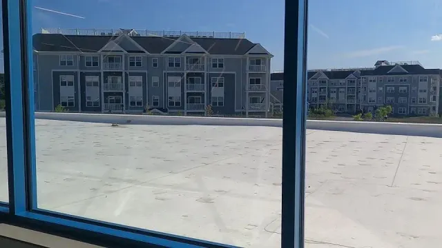 View through a blue window, showing light blue apartment buildings and a white rooftop on a sunny day.