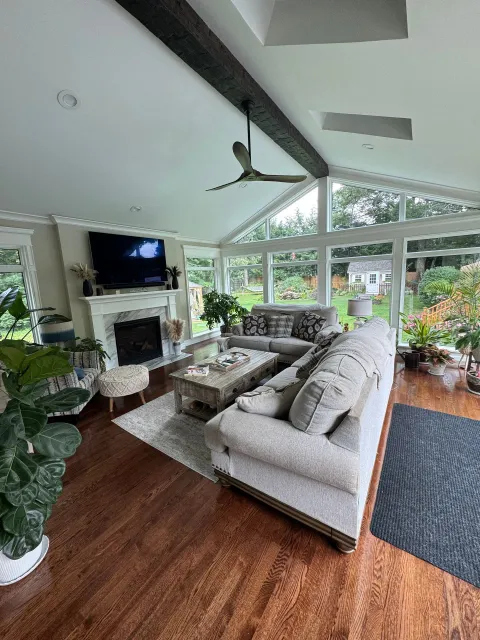 Bright living room with sectional sofa, fireplace, TV, and large windows overlooking greenery