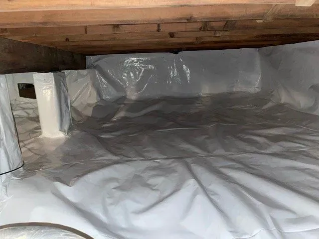 Crawlspace lined with silver vapor barrier under wooden floor joists