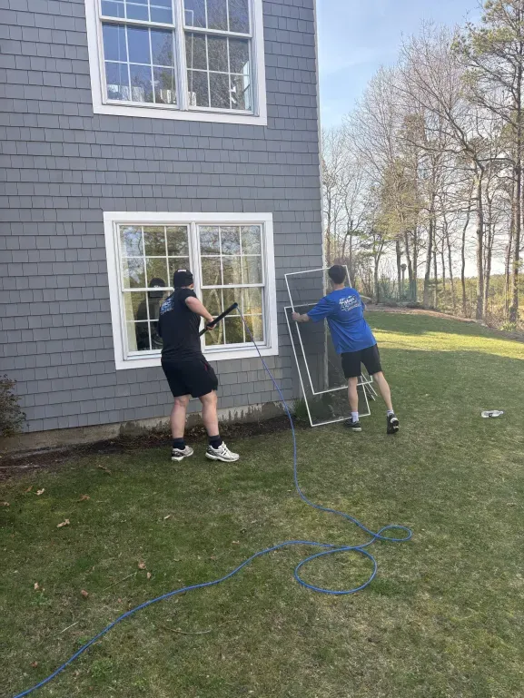 Two Mass Shine crew members removing screens and cleaning exterior windows on shingle home South Shore Massachusetts