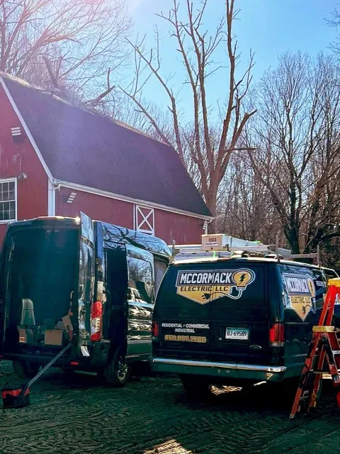 Two McCormack Electric Vans in front of a Red Barn