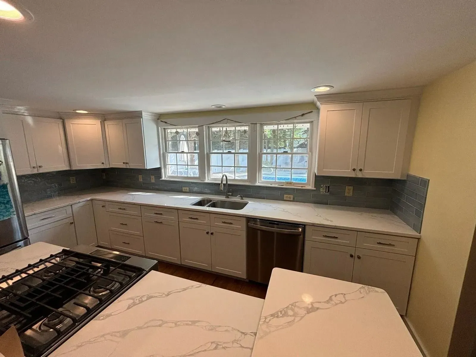 White kitchen with countertops, cabinets, windows, and an island with a gas stovetop.
