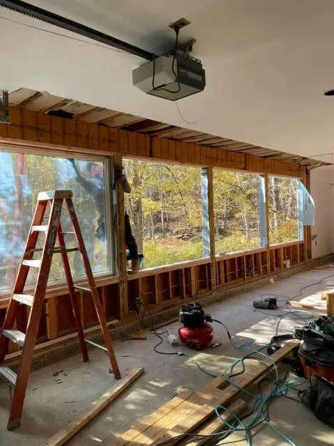 Garage interior renovation: Windows framed, ladder, air compressor, debris on the floor, garage door opener visible.