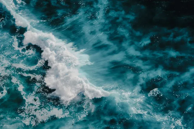 Turbulent ocean water; a wave cresting with white foam, swirling in deep blue.