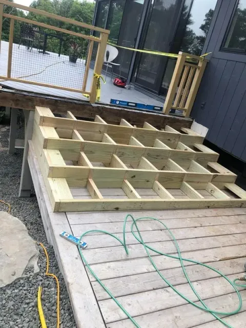 Wooden deck steps under construction with exposed framing. Yellow and green cables are visible.