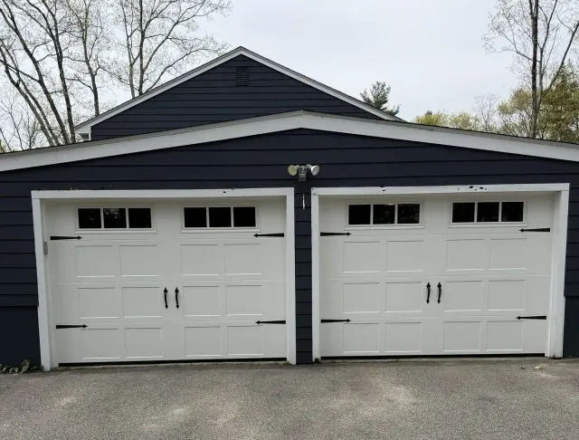 White carriage-style doors with black hardware on a deep blue house