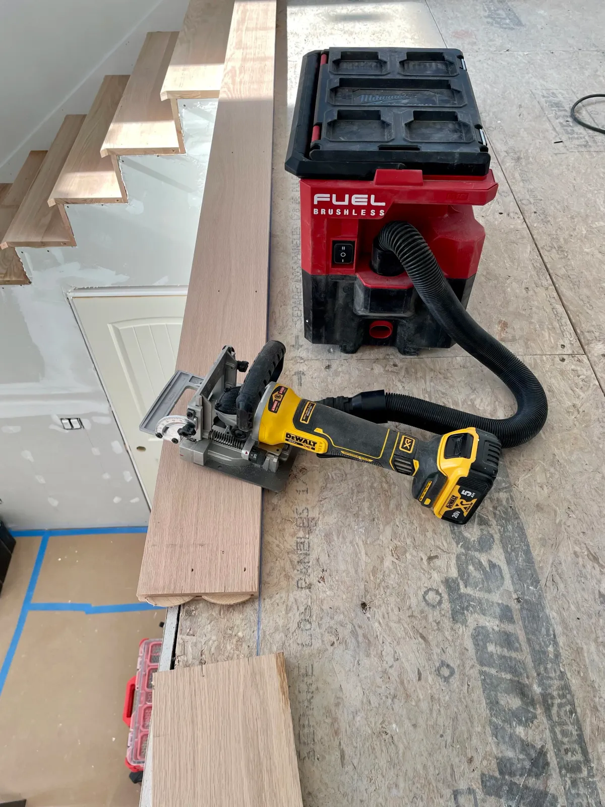 A woodworking workspace with a cordless circular saw, a red shop vacuum, and wooden planks on a workbench.