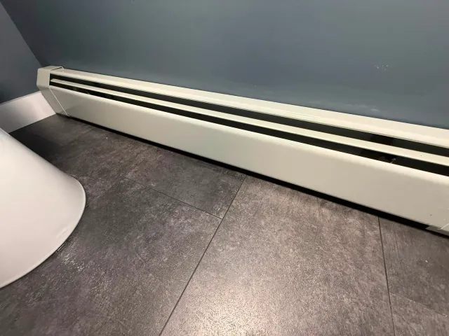 White baseboard heater along a gray wall above dark tile flooring