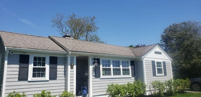 Single-story white house with blue shutters and a front entrance under a clear blue sky