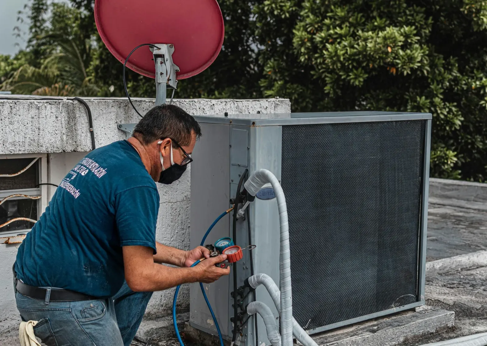 Technician repairing rooftop HVAC unit beside a red satellite dish
