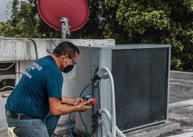 Technician repairing rooftop HVAC unit beside a red satellite dish