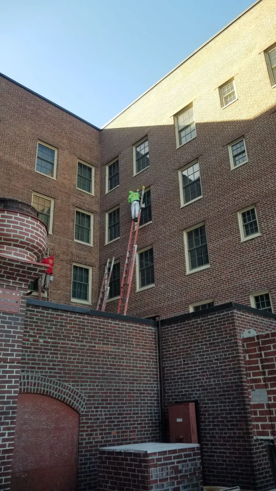 A man on a ladder is painting the side of a brick building.