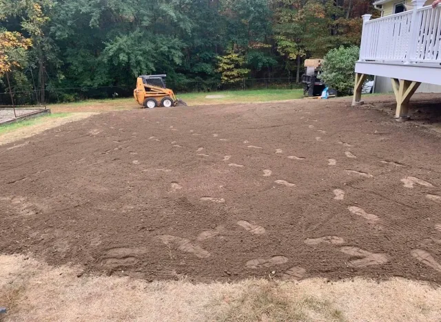 A bulldozer is moving dirt in a backyard next to a deck.