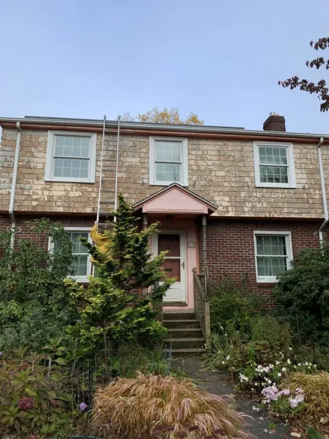 Two-story brick house with a pink front porch, white windows, and a garden in front