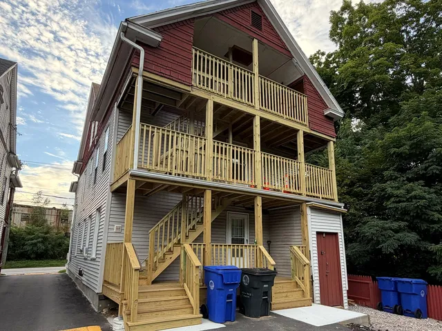 Rebuilt three-story rear porch and exterior stair tower on a multi-family home in Torrington Connecticut, framed in pressure-treated lumber with three stacked landings, full code-height guardrail systems, a switchback stair run down to grade, and new poured concrete pads at the stair bases
