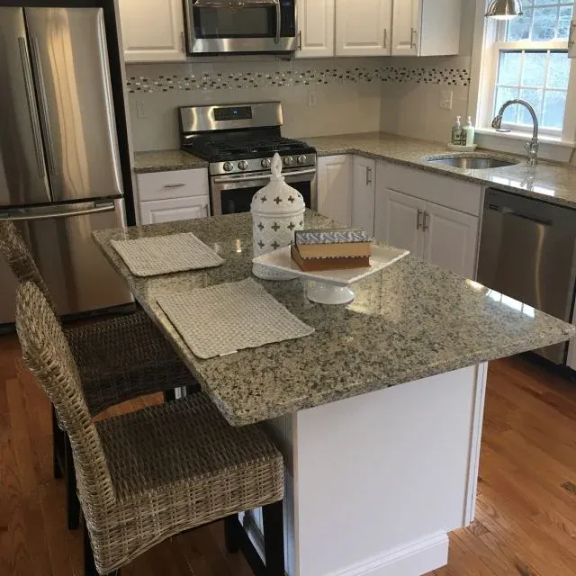 White kitchen with a light granite island, wicker chairs and natural light