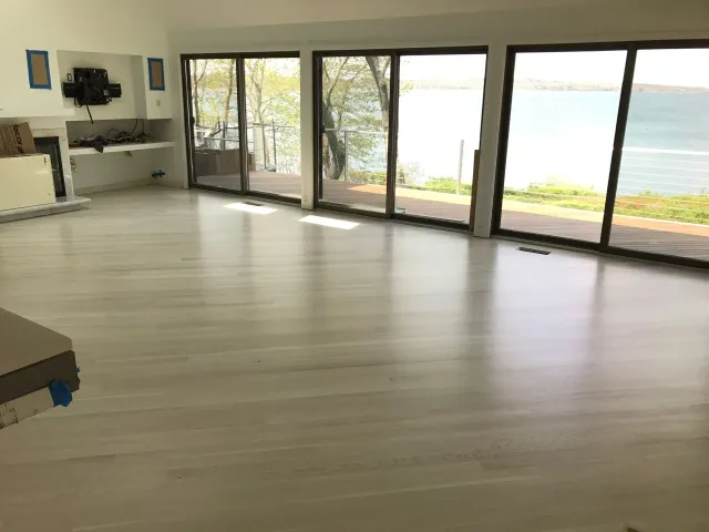 Bright, modern room with light-colored wood floors, large windows overlooking water.