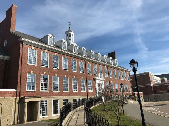 Brick building with many windows, topped with a cupola, under a blue sky with a few clouds.