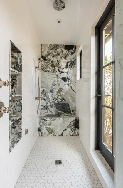 Modern bathroom with walk-in shower featuring a large marble accent wall, white subway tile walls, hexagonal floor tiles, and direct outdoor access for beachgoers.