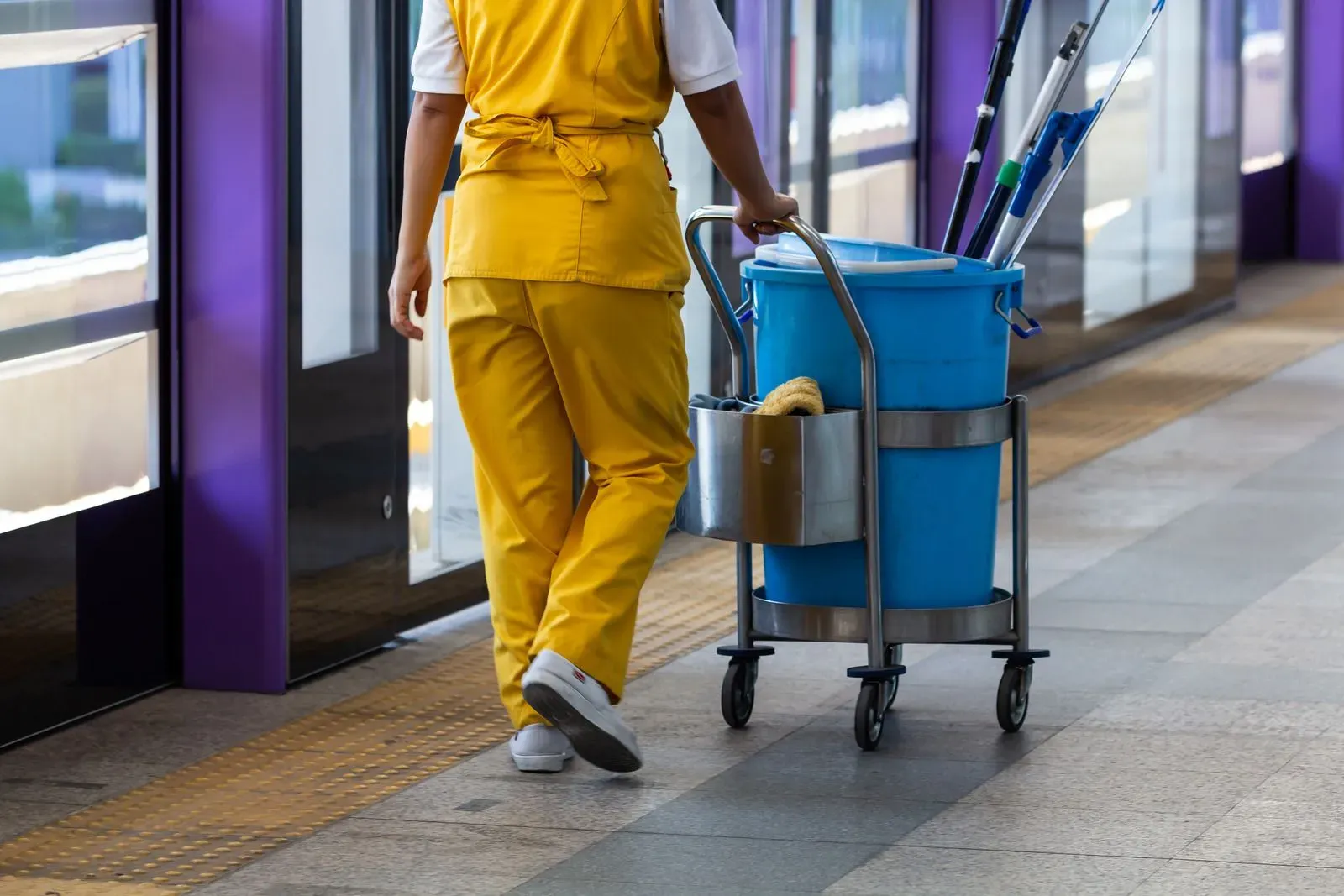 A cleaner is walking with a cart full of cleaning supplies.
