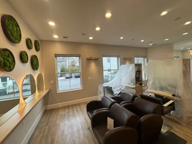 Modern salon interior with black chairs, wood floors, wall mirrors, and covered stations during renovation