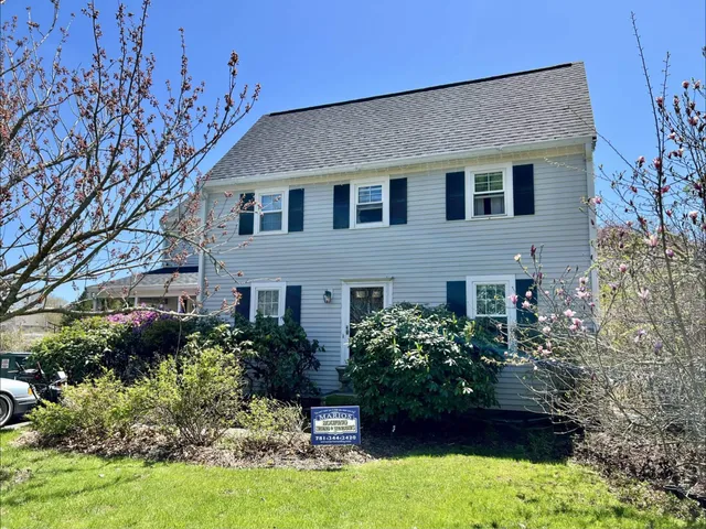 Tan two-story colonial in Sandwich, MA with new CertainTeed Landmark Pro Moire Black roof, black shutters, and blooming magnolia and flowering plum in the front yard