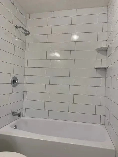 A bathroom with white tile walls and a bathtub.