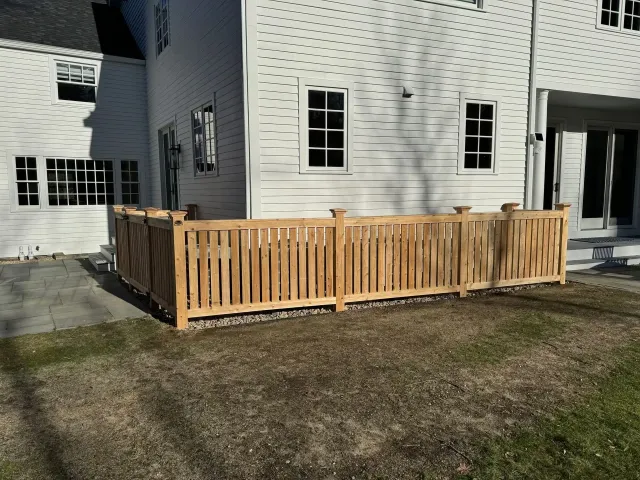 Wooden deck railing around a small patio beside a white house.