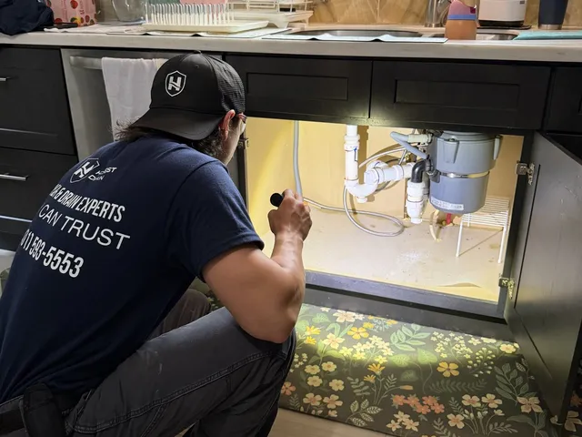Honest Drain technician inspecting piping under a kitchen sink
