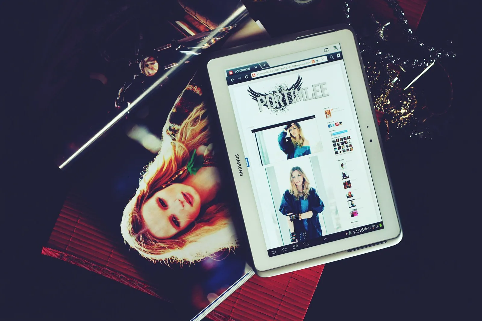 Tablet displaying website, with photo of a blonde woman, lying on a table. Dark background.