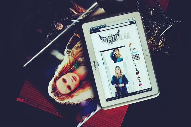 Tablet displaying website, with photo of a blonde woman, lying on a table. Dark background.