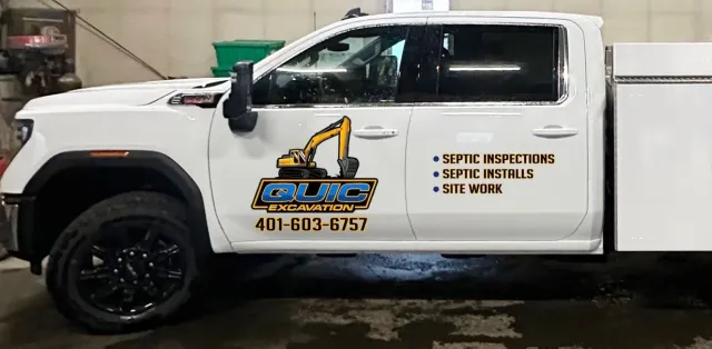 White utility truck with a service body parked indoors, featuring branding on the door for a construction company.