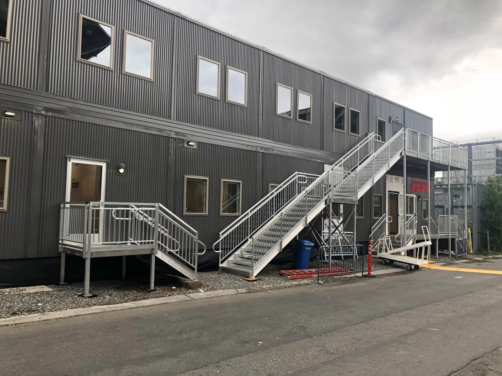 Exterior of a modern building with black corrugated metal siding, multiple windows, and white metal staircases with railings.