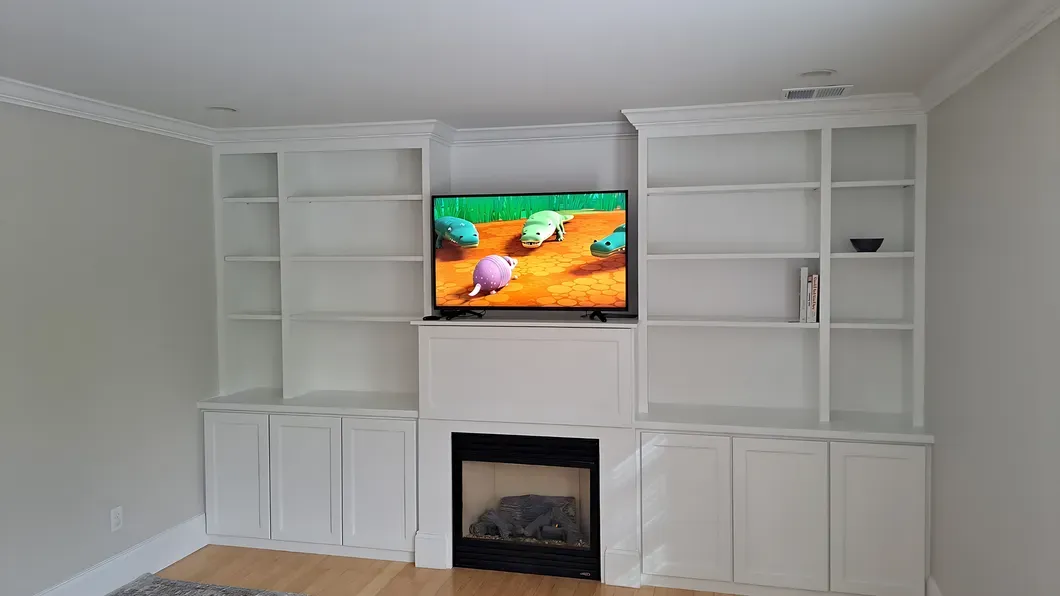 Bright living room with white built-in shelves, a fireplace, and a TV showing a colorful scene.