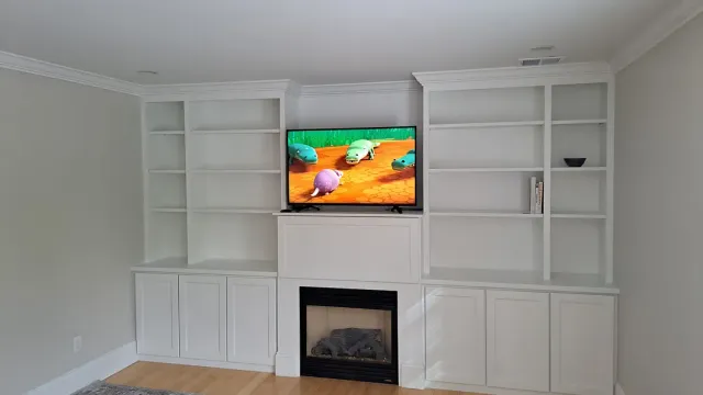 Bright living room with white built-in shelves, a fireplace, and a TV showing a colorful scene.
