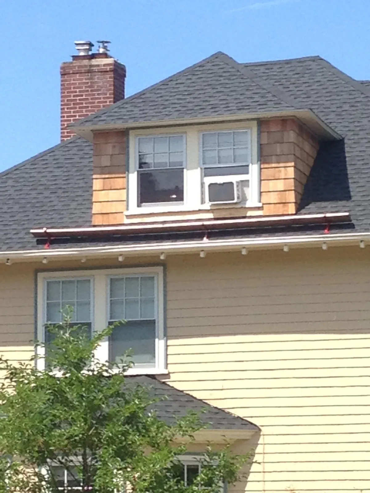 House exterior with tan siding, gray roof, brick chimney, and a dormer window under a blue sky