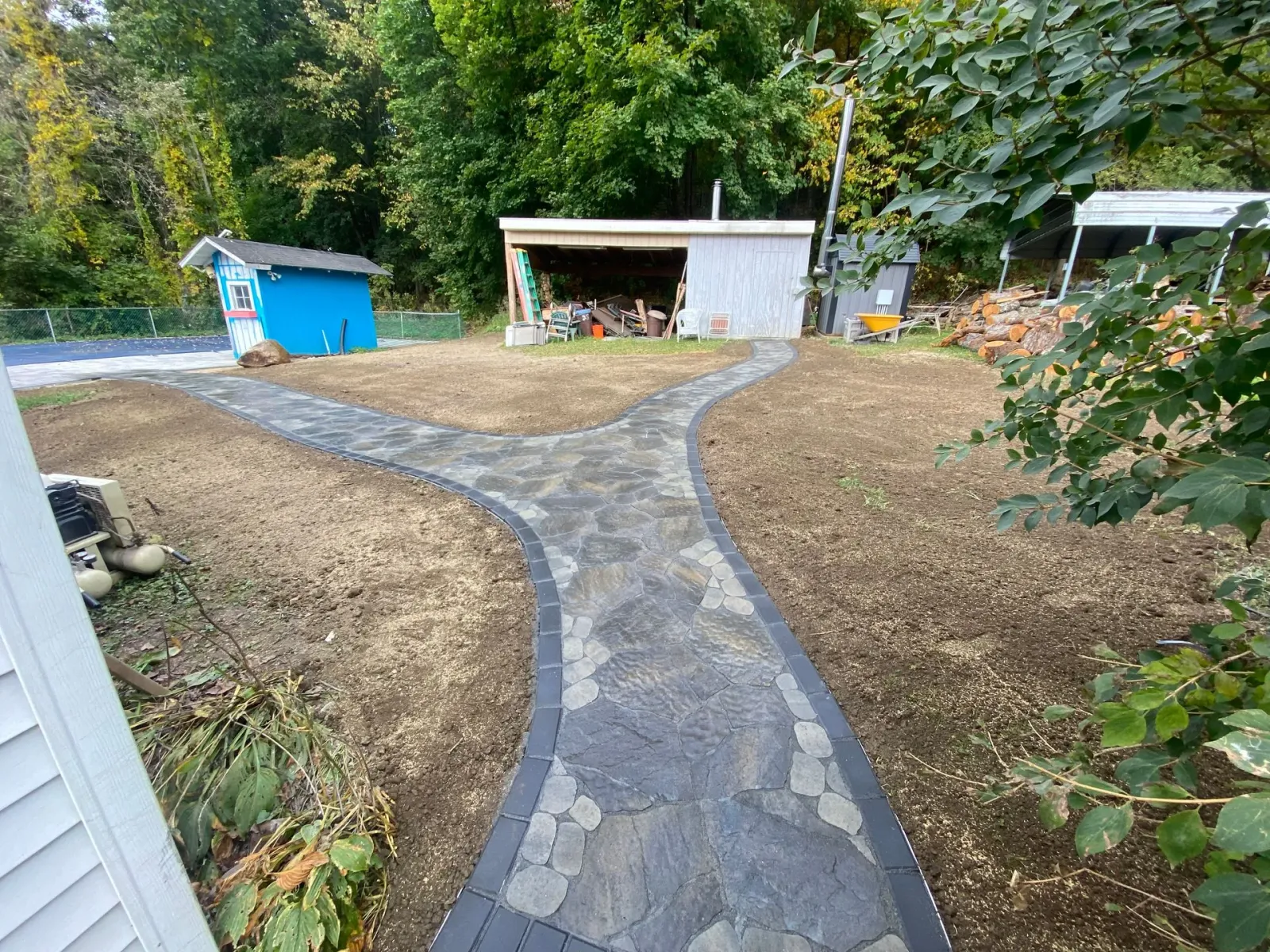 A stone walkway leading to a shed in a backyard.