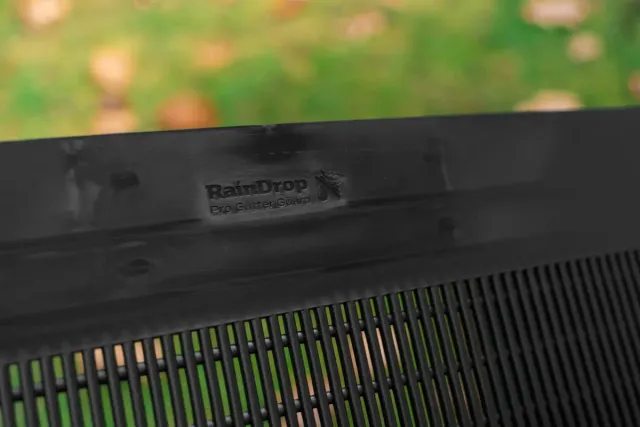 Close-up of black RainDrop Pro Gutter Guard with vertical slats and blurred green background.