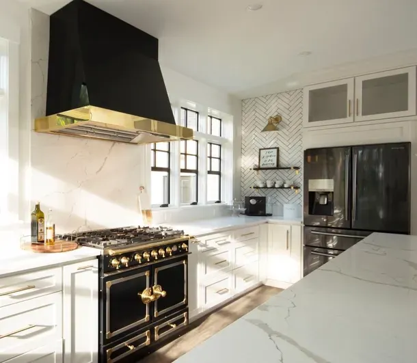 Elegant kitchen with black and gold stove, range hood, and refrigerator. White cabinets and countertops.