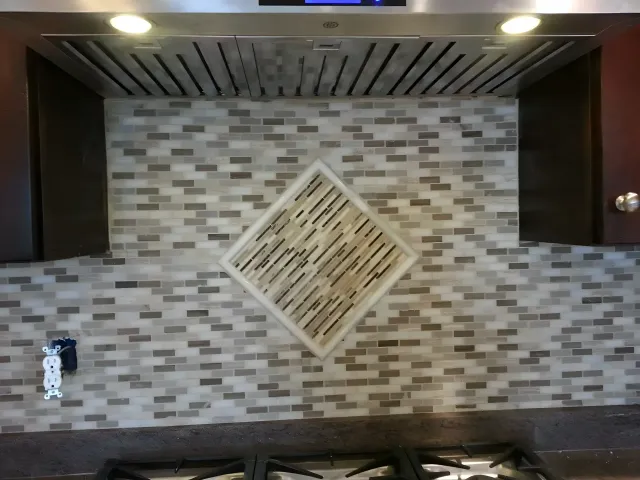 Decorative wall with mosaic tile pattern and recessed lighting above a dark counter.