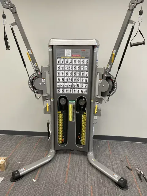 Gym cable machine with yellow weight stacks and multiple pulleys in a workout room