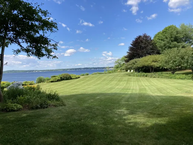 Scenic view of a well-maintained grassy lawn with trees and bushes, overlooking a large body of water.