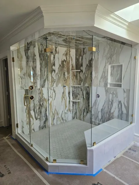 Glass-enclosed marble shower with tiled walls and white base in a bathroom