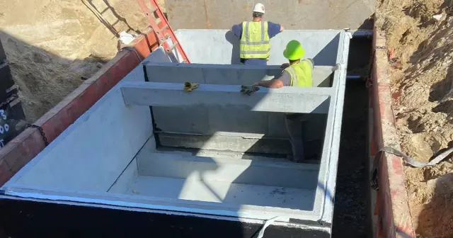 Construction workers installing concrete components in a deep trench.