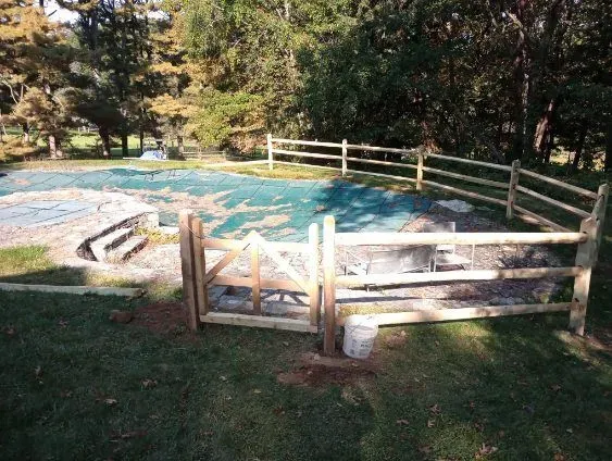 Wooden fence surrounds a pool covered with a green tarp, with a gate, in a grassy yard.