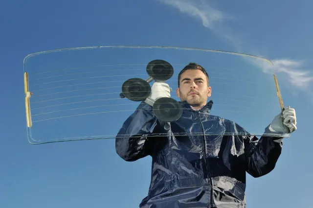 Man holding a curved glass window with suction cups, against a blue sky.